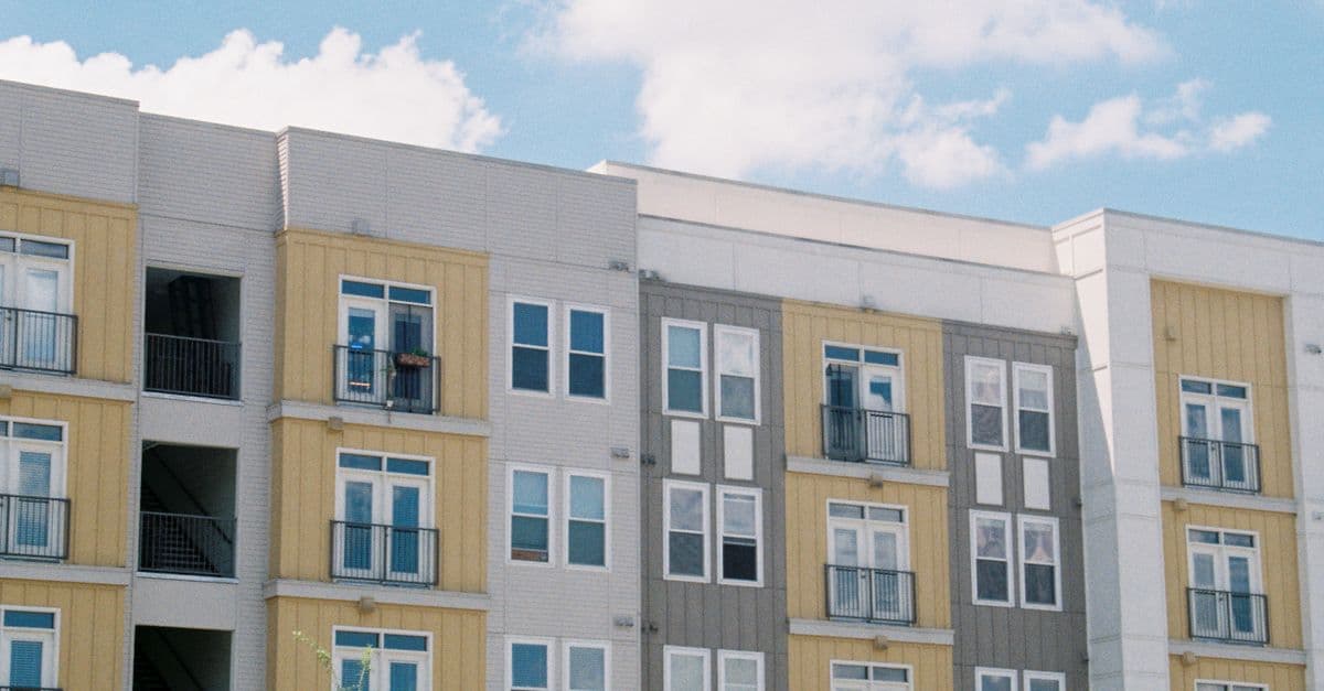 A contemporary apartment building exterior in yellow and grey panels against a clear blue sky.