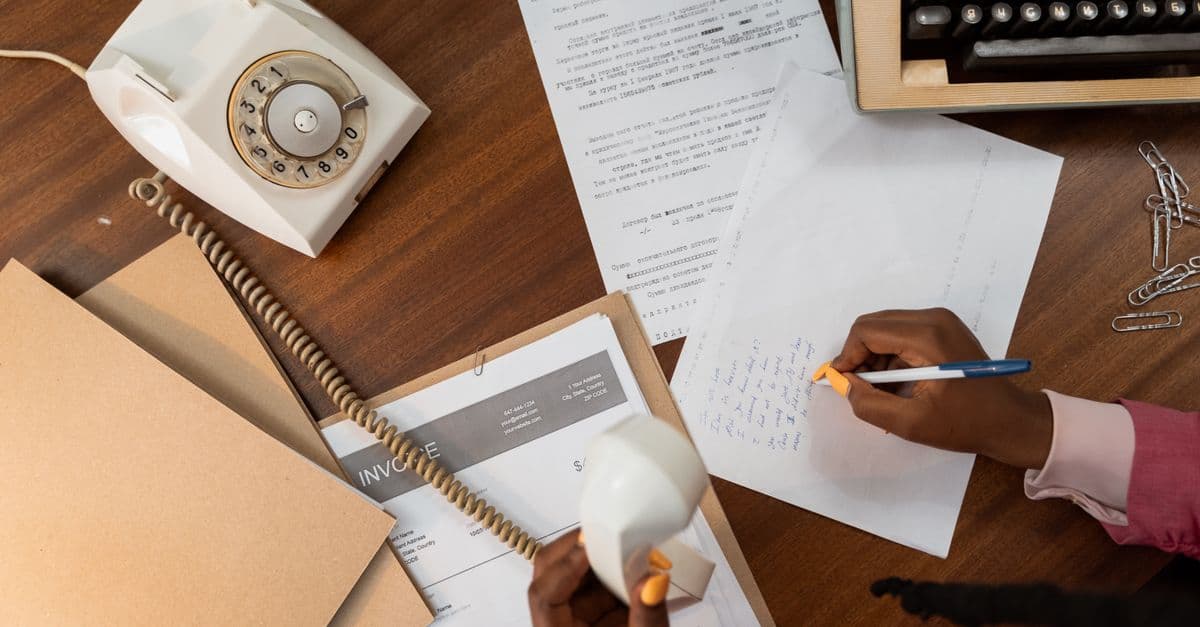 A person holds a phone handset while writing notes on paper at a desk.