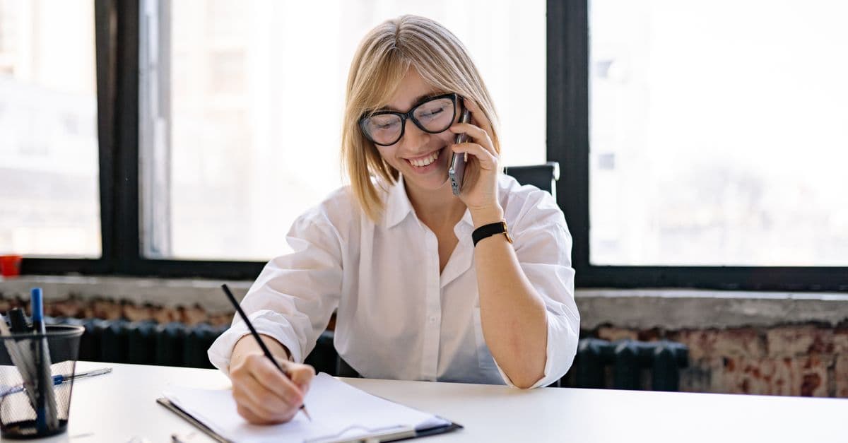 A leasing staff member takes a follow-up call and writes notes at a desk.