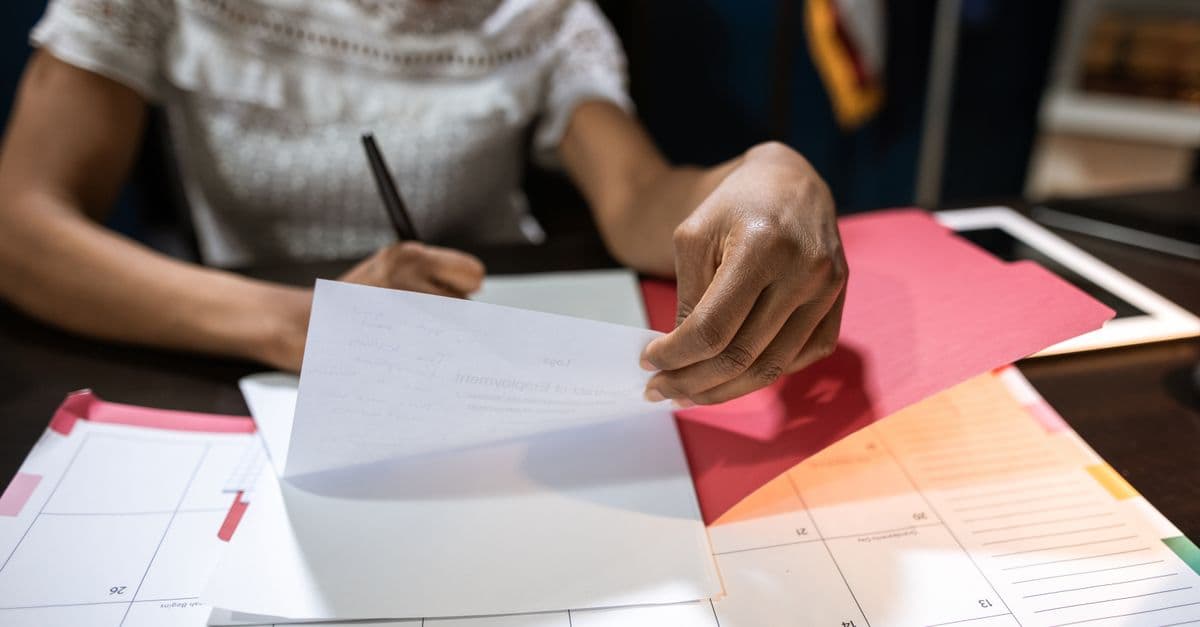 A compliance staffer at a desk cross-checking paperwork against a calendar, tracking certification deadlines.